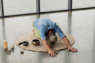 Tibet şarkı kaseleri ve tütsü çubuklarıyla yoga stüdyosunda gerinen gri saçlı adam. 