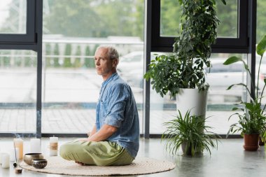 Gri saçlı adam Tibet şarkı kaseleri ve yoga stüdyosunda mum ve meditasyon yapıyor. 