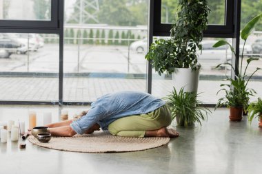 Gri saçlı adam mumların yanında geriniyor ve yoga stüdyosunda Tibet şarkıları söylüyor. 