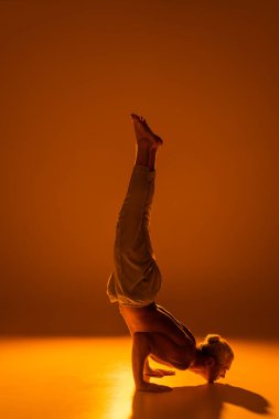 Gömleksiz ve pantolonlu bir adam kahverengi üzerinde çene standı yoga pozu veriyor. 