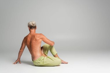 Gri arka planda omurga bükme yoga pozu veren üstsüz bir adamın arka görüntüsü. 