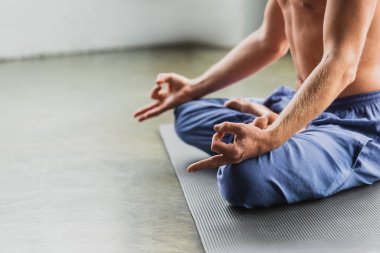 partial view of man in blue pants sitting in lotus pose and doing gyan mudra  clipart