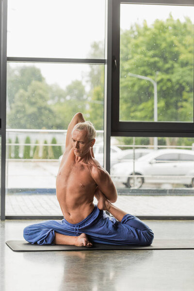 седой мужчина в позе раджакапотасаны на коврике для йоги в студии  