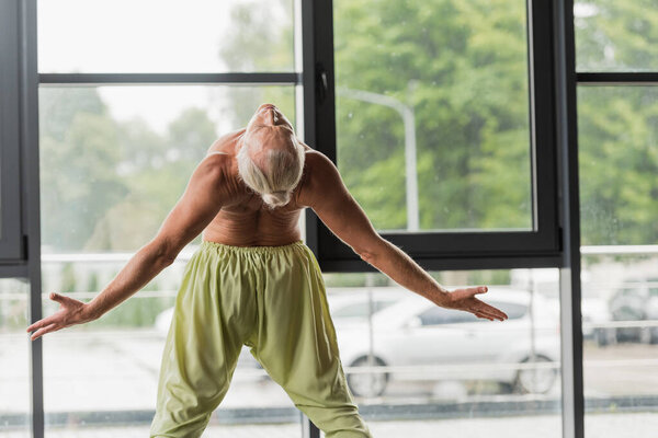 shirtless man in green pants doing backside bend in yoga studio 