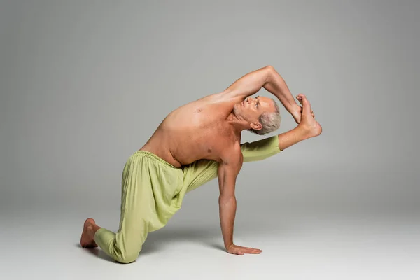 shirtless man in pants doing compass yoga pose on grey background