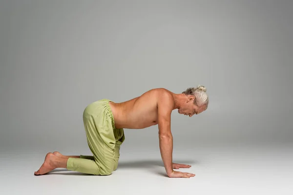 full length of barefoot man in pants doing cow yoga pose on grey