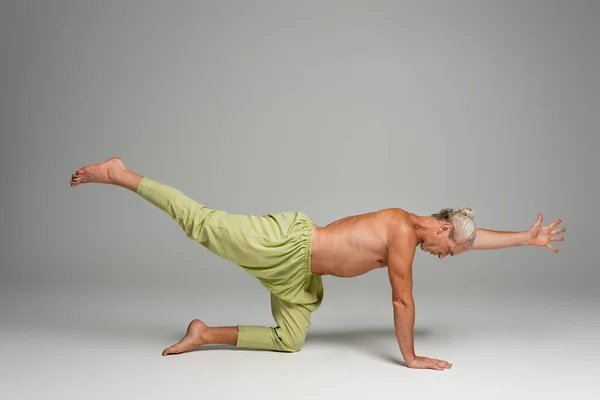full length of barefoot man in pants doing tiger yoga pose on grey