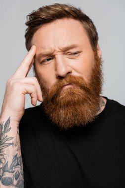portrait of thoughtful bearded man touching forehead and looking away isolated on grey