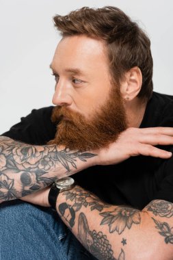 portrait of dreamy tattooed man in black t-shirt and wristwatch looking away isolated on grey