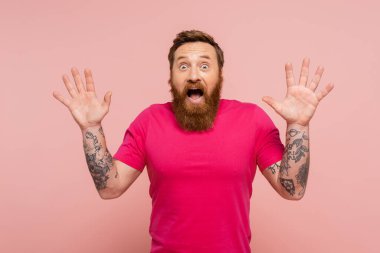 thrilled tattooed man with open mouth showing wow gesture and looking at camera isolated on pink