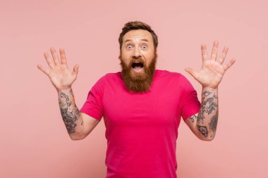 thrilled tattooed man with open mouth showing wow gesture and looking at camera isolated on pink clipart