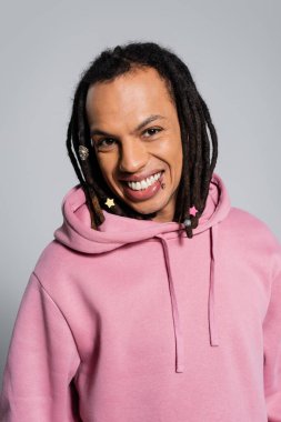 portrait of happy multiracial man with dreadlocks smiling isolated on grey 