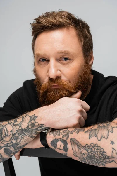portrait of thoughtful tattooed and bearded man looking at camera isolated on grey