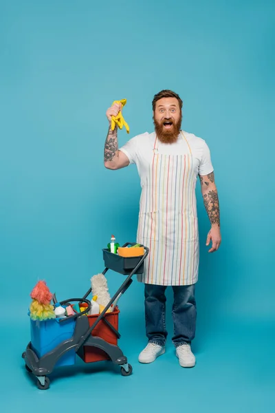 Amazed Bearded Man Apron Holding Rubber Gloves Cart Cleaning Supplies — Foto de Stock
