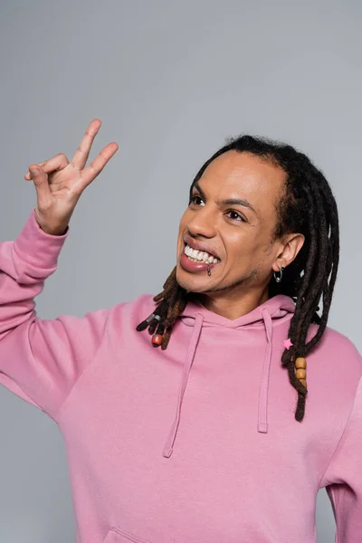 stock image positive multiracial man with dreadlocks showing peace sign isolated on grey 