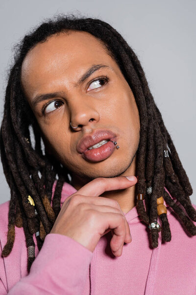 portrait of pensive multiracial man in pink hoodie looking away isolated on gray 