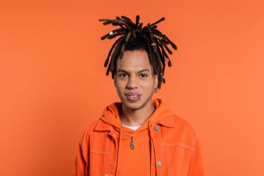 portrait of pierced multiracial man with dreadlocks looking at camera isolated on coral background 