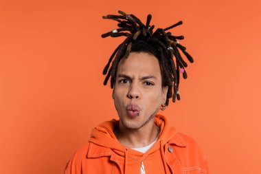 portrait of pierced multiracial man with dreadlocks pouting lips isolated on coral background 