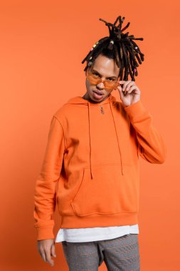 multiracial man with dreadlocks adjusting stylish sunglasses on coral background 