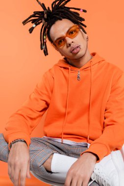 multiracial man in trendy sunglasses looking at camera isolated on coral 
