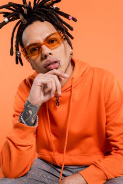 tattooed multiracial man with dreadlocks and stylish sunglasses isolated on coral 