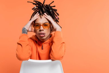 focused multiracial man with dreadlocks and stylish sunglasses isolated on coral background 