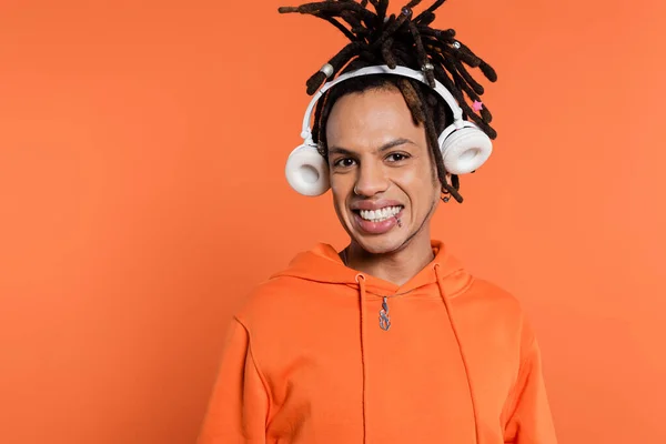 stock image funny multiracial man with dreadlocks and wireless headphones isolated on coral 