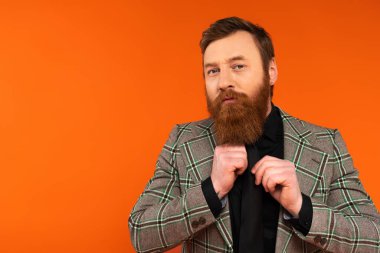 Bearded man in checkered jacket looking at camera isolated on red 