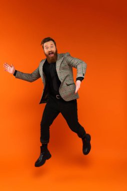 Excited stylish man jumping and looking at camera on red background 