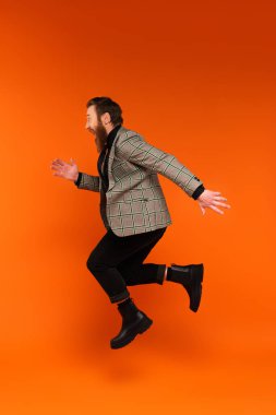 Side view of excited stylish man jumping on red background 