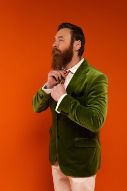 Fashionable bearded man adjusting tie isolated on red  clipart