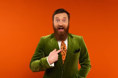 Excited bearded model in jacket pointing with finger at himself on red background 