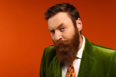 Focused bearded man in green blazer looking at camera on red background 