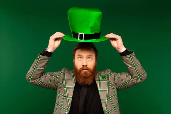 stock image Bearded man in jacket looking at hat during saint patrick celebration isolated on green 