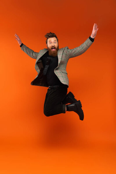 Amazed bearded man in plaid jacket jumping on red background 