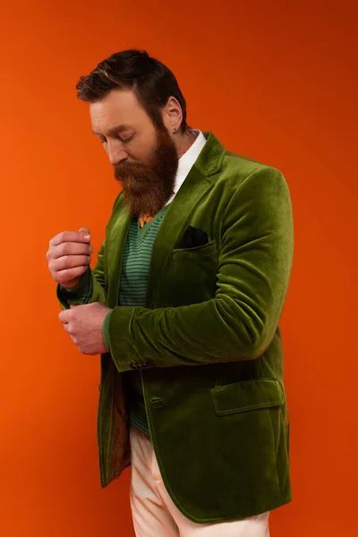 Trendy bearded model adjusting sleeve of jacket on red background