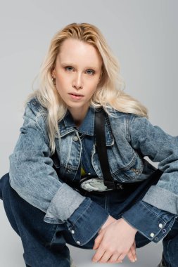 blonde albino woman in stylish denim jacket with belt bag posing isolated on grey 