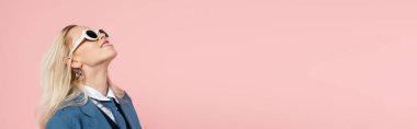 cheerful blonde woman in blue blazer and sunglasses smiling isolated on pink, banner 