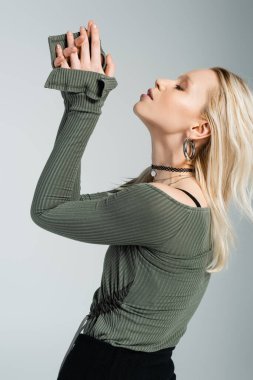 side view of blonde woman in long sleeve shirt and black skirt posing isolated on grey 