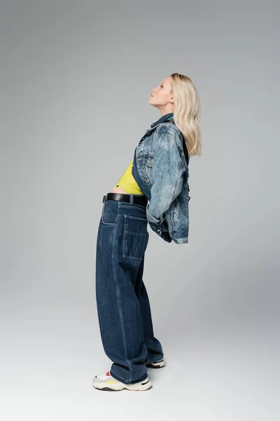 stock image full length of young blonde woman in stylish denim outfit posing on grey 