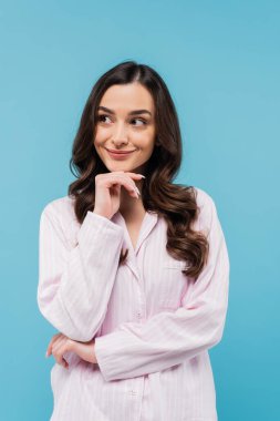 smiling young woman in sleepwear looking away isolated on blue 