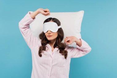 Pijamalı ve gece maskeli genç bir kadın. Mavi yastığın yanında uzanıyor.