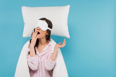 Gece maskeli genç bir kadın mavi yastığın yanında esniyor. 