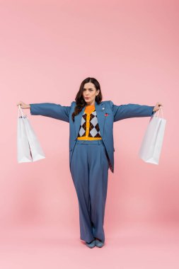 full length of tired woman in blue pantsuit holding shopping bags and breathing deeply on pink  clipart