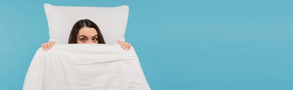 stock image young woman in pajamas covering face with warm duvet near pillow isolated on blue, banner 