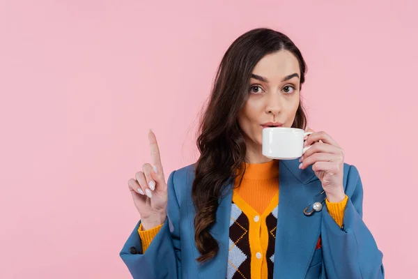 stock image brunette woman in blue blazer drinking coffee and showing wait gesture isolated on pink 