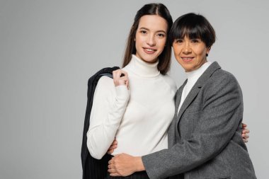 Asyalı anne ve kız zarif giysiler içinde. Gri renkli kameraya sarılıp bakıyorlar.