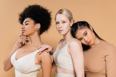 young interracial models in underwear looking at camera near curly african american woman isolated on beige