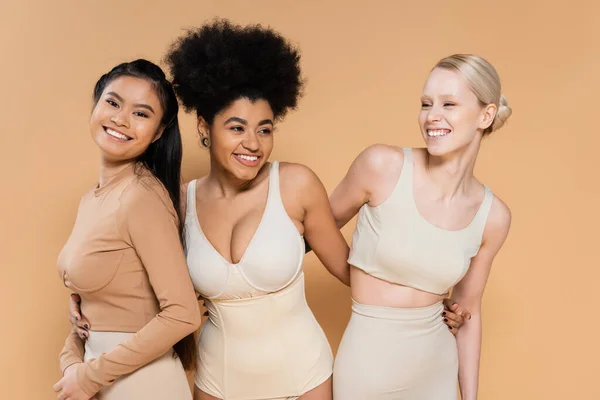 stock image cheerful african american woman in lingerie embracing young multiethnic models isolated on beige