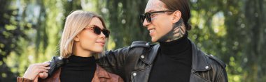 happy tattooed man in sunglasses hugging girlfriend in leather jacket, banner 